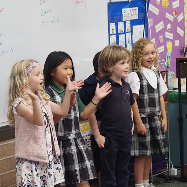 Four students singing and clapping at the front of a classroom