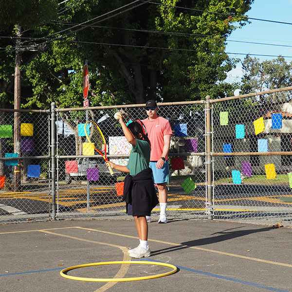 A student stands at-bat during gym class, holding a tennis racket