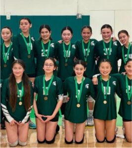 A volleyball team in a gymnasium, wearing matching medals.